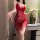 Woman wearing red lace babydoll sleepwear with sheer mesh and adjustable straps, posing indoors near a vase of flowers.