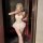 Woman in white nightsigh lace corset bodysuit with boning, puff skirt, and thigh-highs, holding champagne while taking mirror...