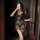 Woman in black lace babydoll dress holding phone and wine glass, showcasing sheer design and adjustable drawstring detail.