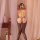 Woman wearing nightsigh black lace mesh bodystocking with open crotch and sheer stockings, viewed from behind.
