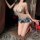 Woman kneeling in sheer nightsigh nightseduce bodysuit with denim shorts, holding wine glass in dimly lit room.