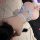 Woman wearing white lace bodysuit with sheer mesh and open-crotch design, lying on bed with fluffy blanket and rose petals ne...