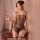 Woman in black sheer mesh bodysuit with open-crotch and peekaboo bust, holding mirror beside wooden nightstand.