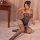 Woman wearing black nightsigh nightsere sheer mesh bodysuit with open-crotch and peekaboo bust, seated on bed.