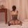 Woman wearing nightsigh black sheer mesh bodysuit with open back and crotch, seated on bed in romantic bedroom setting.