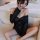 Woman wearing black sheer off-shoulder nightsigh lingerie set with snowflake-style chemise, seated on sofa.