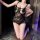 Woman kneeling in black lace bodysuit with floral trim, sheer mesh, and open-crotch design.