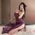 A woman poses in a purple lace cami dress with side slits, capturing a selfie while wearing black heels and red flower access...