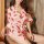 A woman wearing a sheer chiffon kimono robe adorned with red lips patterns, tied at the waist, sitting against a rustic woode...