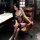 Woman in pearl-embellished sensual open-crotch bodysuit, seated on leather chair — sexy, playful lingerie with sheer polka-do...