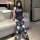 A woman poses on a couch wearing a black bodysuit with spiderweb patterns and white heart designs on matching stockings, perf...
