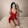 Woman in red lace lingerie set kneeling on bed, showcasing plus size busty sleepwear with sheer fabric and delicate straps.