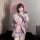 Woman in pink sheer kimono lingerie set with bow print, holding parasol and phone, posing indoors.