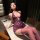 A woman poses elegantly wearing a sheer lace bodysuit paired with purple stockings, highlighting a seductive design perfect f...