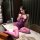 A woman poses on a table wearing a purple sheer lace bodysuit paired with pink stockings, showcasing a seductive sleepwear de...