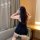 A woman wearing a black lace-trimmed maid costume, sitting on a couch adjusting her hair accessory. the outfit features a plu...