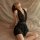 Woman in black deep v neck sleep dress with sheer mesh back, elegant plus size lingerie set on soft bed.