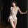 Woman modeling white lace bodysuit with ruffled straps and open-crotch design, featuring embroidered floral details and push-...