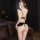 Woman wearing black lace bodysuit with open-crotch design and push-up cups, shown from back in dimly lit room.