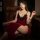 A woman sits elegantly on a leather chair wearing a luxurious red lace cheongsam lingerie set, featuring intricate black lace...