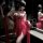 Woman wearing red sheer lace sleep dress with vintage embroidery, holding matching lingerie in dimly lit room.