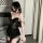 Woman wearing black lace sleepwear set with sheer details and ruffled hem, posing in bedroom setting.