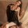 Woman wearing black sheer open-crotch nightgown with bow and peekaboo bust design, seated on vintage chair.