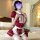 A person wearing a red and white maid costume set, featuring a ruffled dress, apron, and stockings, sitting on a bed with a h...