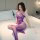 Woman wearing purple plus size sexy mesh lingerie set with sheer lace bodysuit and fishnet stockings on bed.