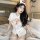 Woman in white nurse lingerie set with lace-up front, hollow-out design, and fishnet stockings on bed.