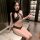 Woman wearing black lace halter bodysuit with rhinestone chain, holding wine glass in modern room.