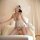 Woman wearing pure & alluring pearl lace sheer sleep dress with deep v mesh and pearl details, posing elegantly on bed.