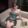 A woman poses elegantly on a couch wearing a sensual, minimalist green bralette set with floral embroidery and delicate fring...