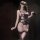Woman in black and purple lace bodysuit with bows, pearls, thigh-highs, holding a feathered mask—pure & playful lingerie set.