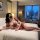 Woman in pink pure & playful lingerie set on hotel bed, featuring cute student-style open-crotch bodysuit with hook closure.