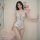 A woman poses next to a pink teddy bear wearing a floral lace bodysuit from pure & playful, featuring adjustable straps and n...