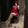 A woman poses in a red sheer dress with lace sleeves, sitting on a stool while taking a mirror selfie. the outfit features a ...