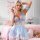 Woman in blue lace lingerie dress with waist cinching, holding pink phone in playful princess-style bedroom setting.