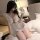 A woman sits on a bed wearing a sheer sleep dress with ruffled details, holding a matching accessory. the outfit features del...