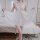 Woman wearing white sheer lingerie sleep dress with lace detailing, standing in bedroom holding flowing fabric of romantic ni...