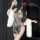 Woman wearing sheer ink-wash qipao lingerie set with white fur stole, holding fan, red rose in hair.