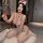 Woman in red and white heart polka dot nurse bodysuit with lace trim, bow headpiece, and stethoscope, kneeling on fluffy rug.