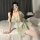 A woman poses on a bed wearing a sheer green lace dress set, featuring delicate ruffles and stockings, perfect for cosplay or...