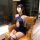 A woman sits in an armchair wearing a navy blue lace halter airline uniform set, featuring a deep cut and thigh-high stocking...