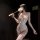 Woman in white lace bodysuit with sheer panels, removable cups, and matching thigh-high stockings holding a feather wand.