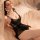 Woman wearing black lace mesh cami sleep dress with embroidered details, sheer fabric, and flirty silhouette on soft bed.
