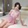 Woman in pink satin-blend sleep dress with lace trim and adjustable straps, posing on bed.