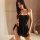 Woman wearing black sheer oversized nightdress with backless design, sitting on bed in elegant bedroom setting.