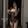 Woman in black sheer lingerie with open-crotch design, featuring lace trim and polka dots, posing for mirror selfie.