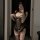 A woman poses in a mirror wearing a black lace lingerie set with sheer fabric, featuring an open design and ruffled details, ...